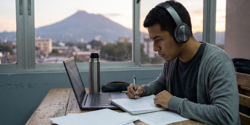Joven salvadoreño practica con audífonos frente a una laptop para el TOEFL en El Salvador